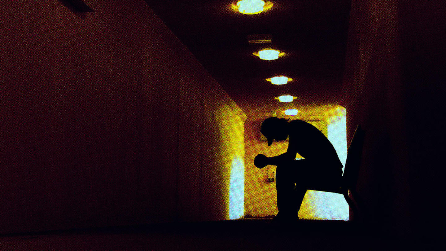 A person sitting in a chair hunched over in a dark hallway