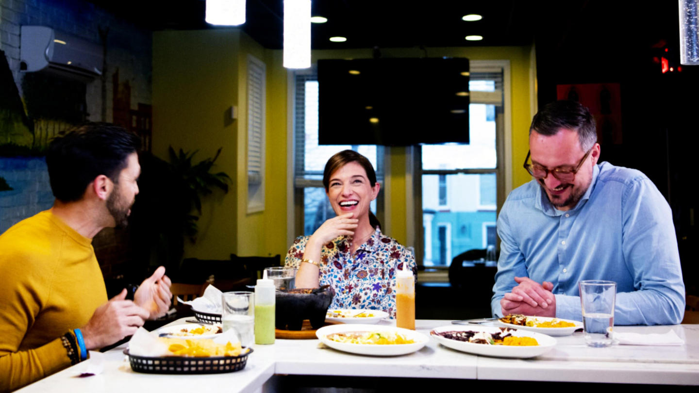 Three people, including Pati Jinch, sit at a counter eating food