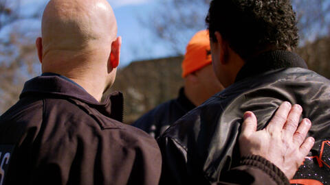 Two men seen from behind; one man has his hand on the other one's back