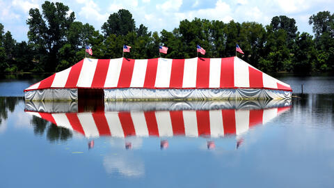 A red-and-white striped tent with American flags sits by a serene lake, symbolizing a family business rooted in tradition and community.