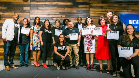 People at a "HUSTLE PHX" event pose with certificates, celebrating completion.
