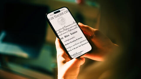 Person holding a phone with teaching credential visible on the phone screen.