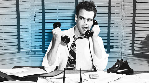 Man in an office holding two phones.