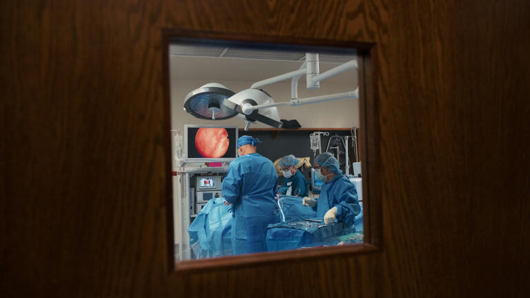 Looking into a operating room full of workers.