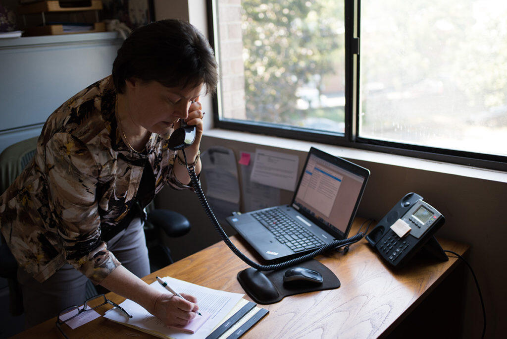 Heather Lynskey talks on the phone and takes notes while standing at her desk