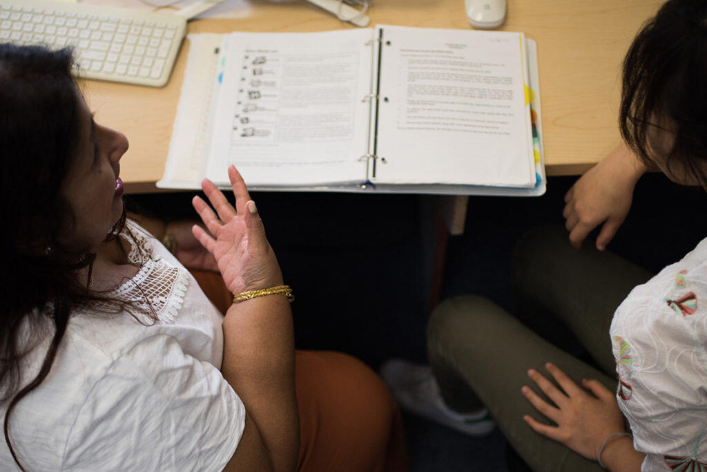 A teacher looks at materials in a binder with a student